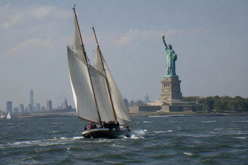A schooner heeling under sail on the Hudson River with the Statue of Liberty in the distance