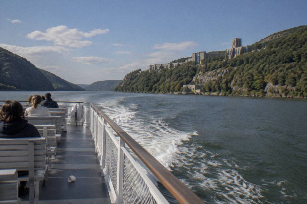 Wooded hillsides rising above wide river water with a tour boat wake trailing behind