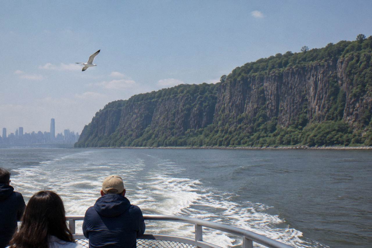 A sightseeing boat traveling north on the Hudson River with forested palisades on the far shore