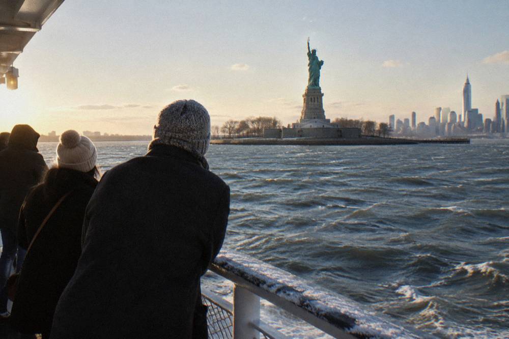 Passengers on a cruise deck looking toward the Statue of Liberty across open water