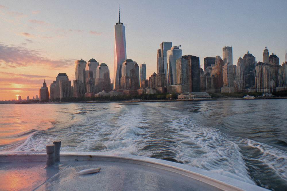A cruise boat passing the Lower Manhattan skyline at golden hour