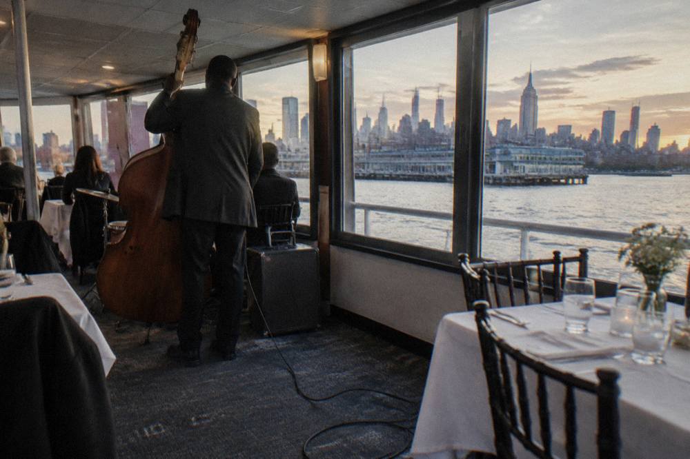 Set dinner tables with white linen beside tall windows on a cruise ship deck at dusk
