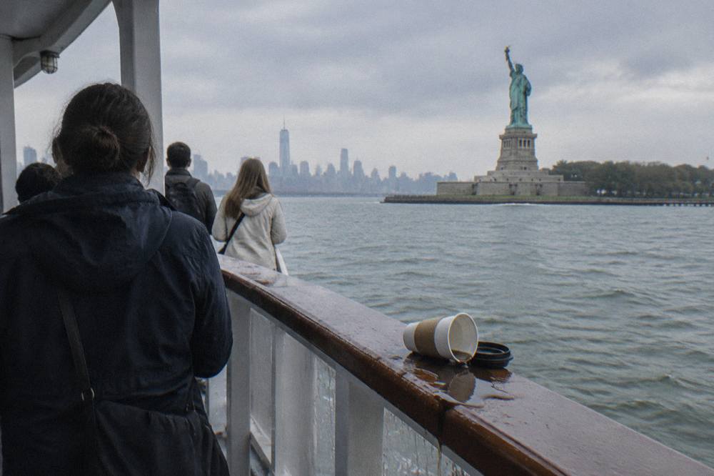 Passengers on an open deck of a sightseeing boat looking toward the Statue of Liberty across the harbor