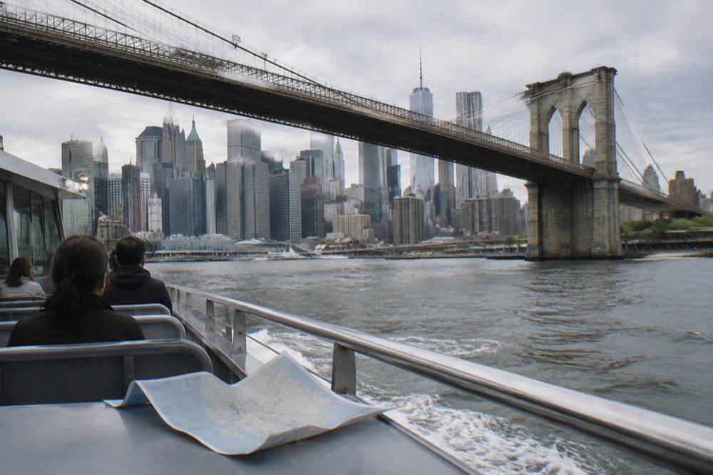 A large sightseeing boat passing the Brooklyn Bridge with the Lower Manhattan skyline in the background