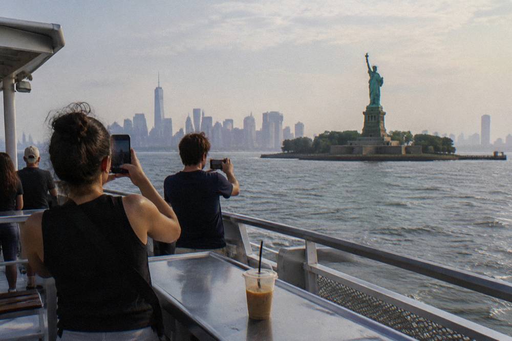 Passengers on an open deck of a cruise boat photographing the Statue of Liberty from the water