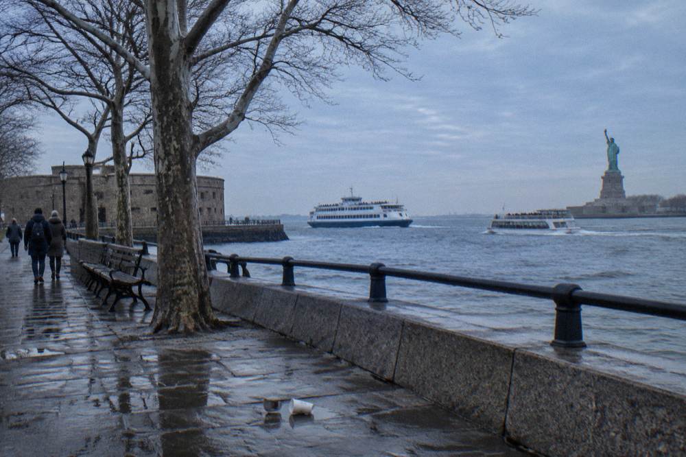 A ferry boat and a sightseeing cruiser crossing New York Harbor near the Statue of Liberty at midday