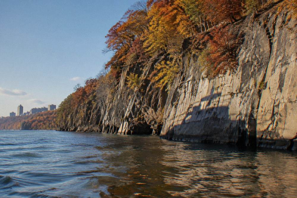 Autumn hardwoods in orange and red above a rock cliff face at the waterline