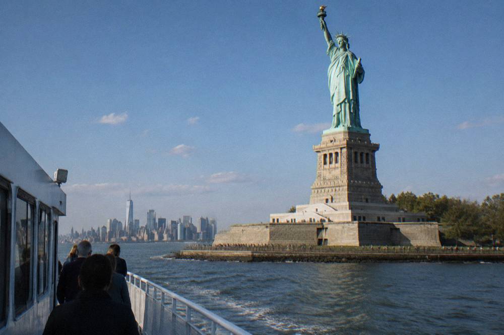 A small sightseeing boat passing close to the Statue of Liberty in open water