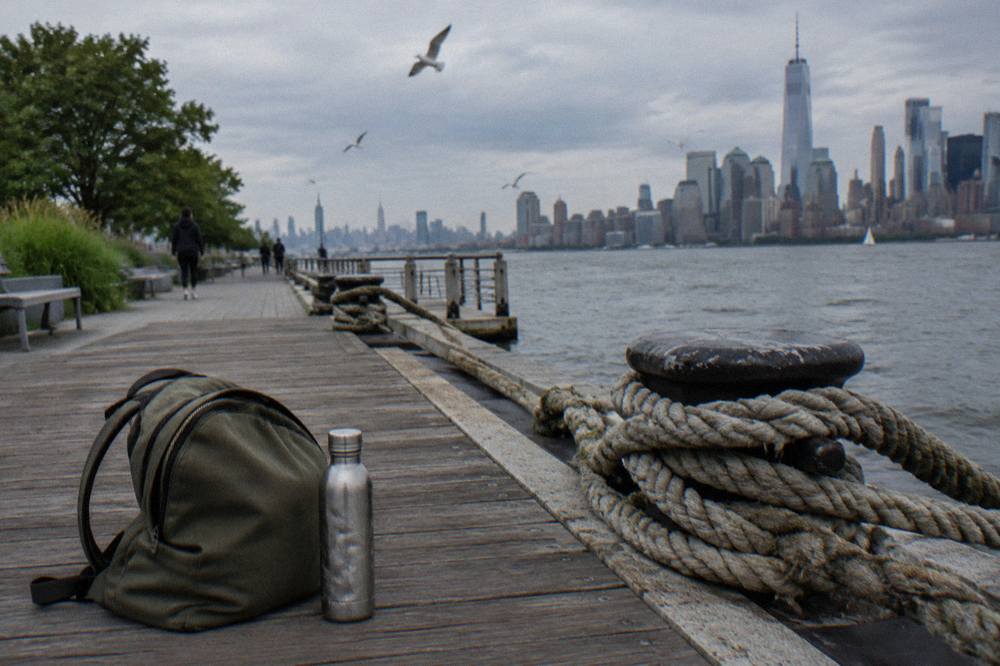 Closed soft daybag and water bottle resting on a wooden pier bench beside mooring lines