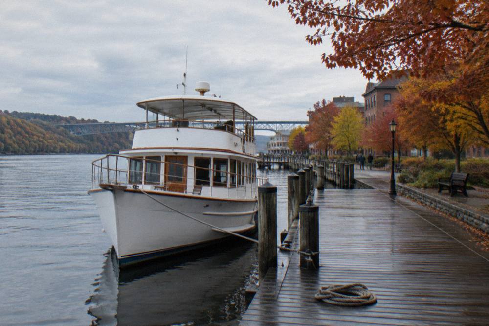 A wooden yacht on the Hudson River in autumn with red and gold trees along the shoreline