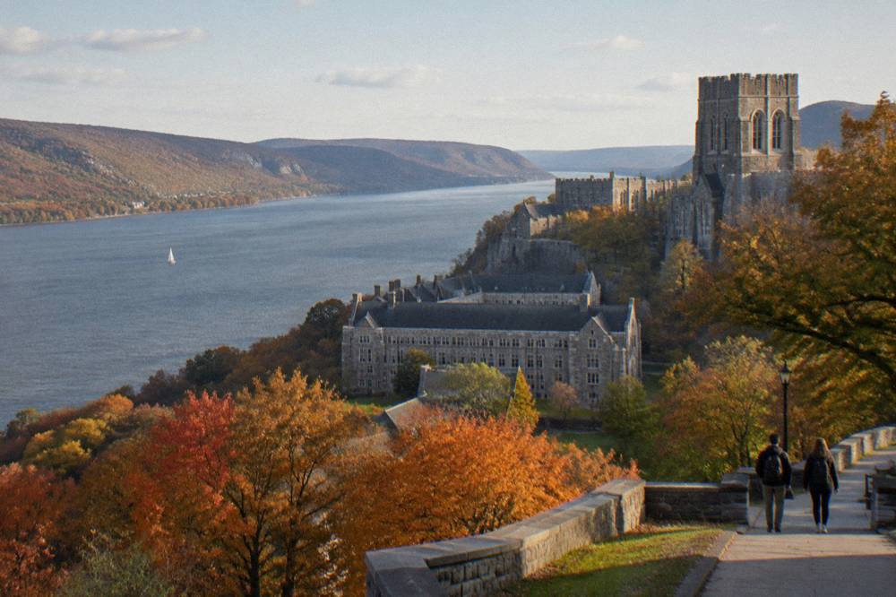 Autumn hillsides in red and orange above a wide reach of the Hudson River north of the city