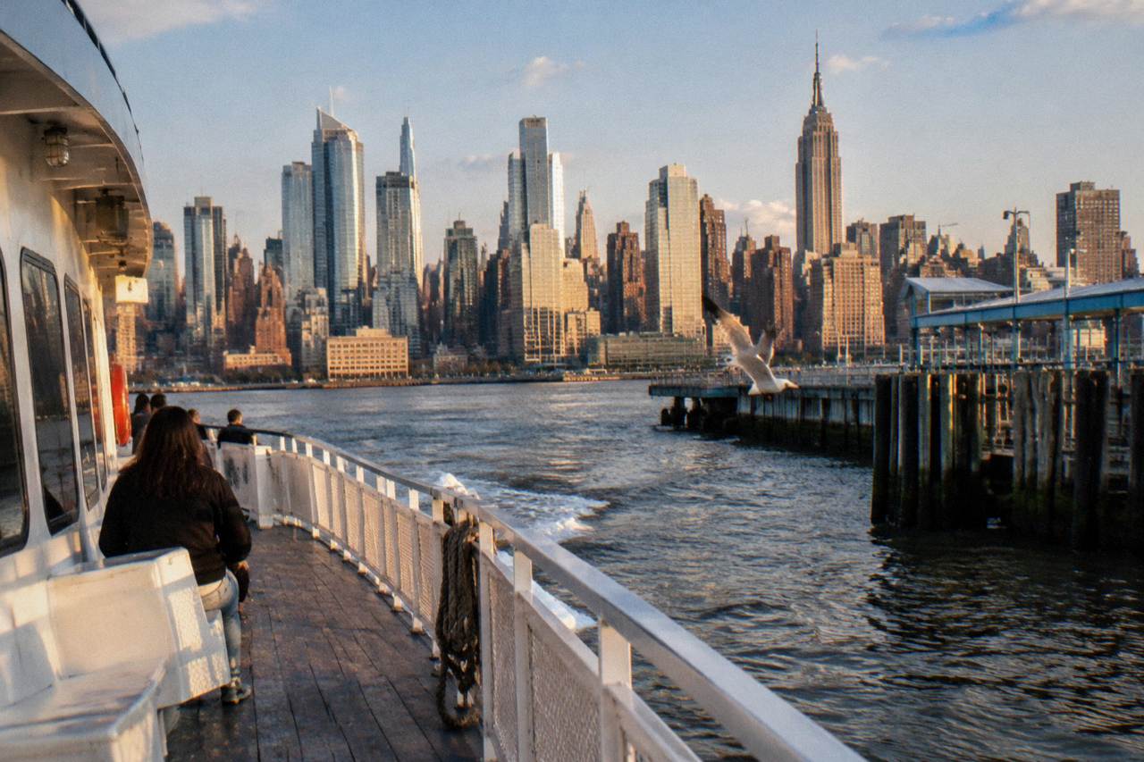 A sightseeing boat on the Hudson River with the Manhattan skyline behind it at golden hour