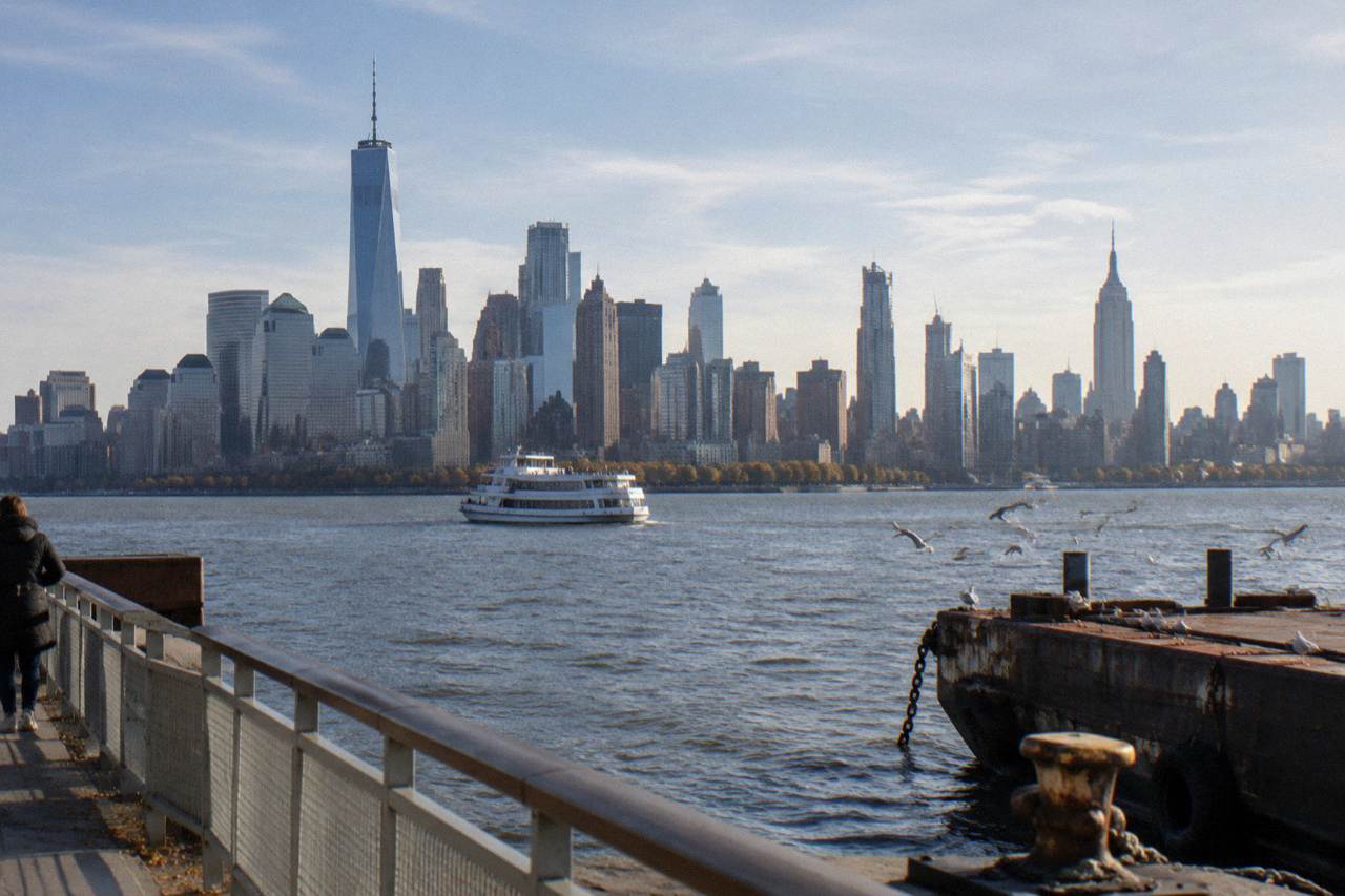 A sightseeing boat on the Hudson River with the Manhattan skyline behind it under a wide sky