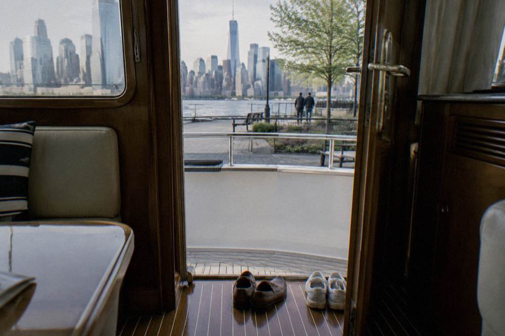 A row of dress shoes and neat casual shoes lined up at the doorway of a yacht cabin with polished wood flooring