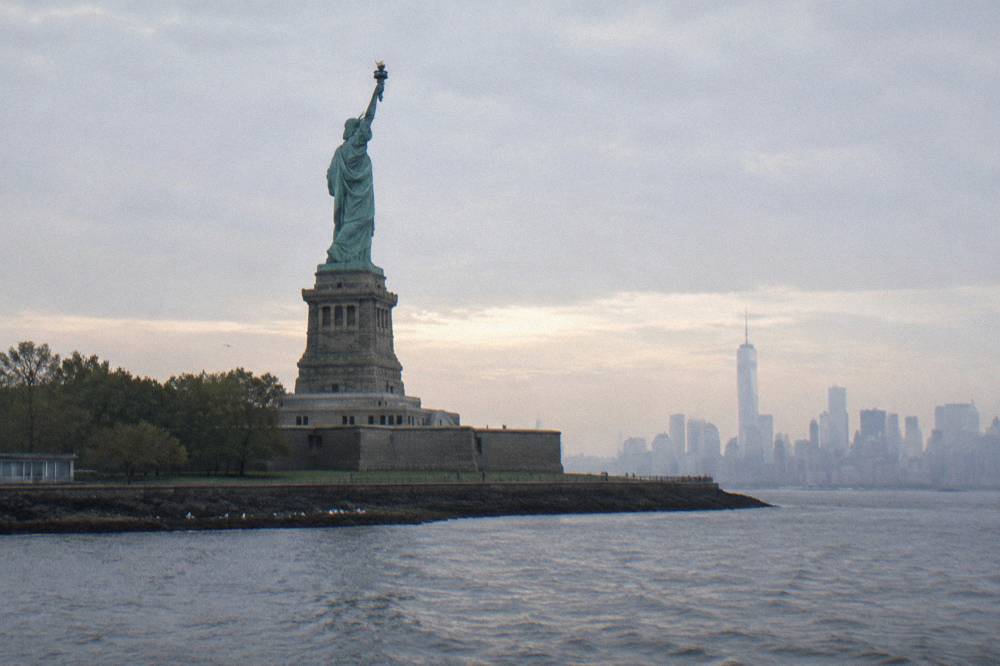 Liberty Island and the Statue seen from open harbor water with the Manhattan skyline beyond