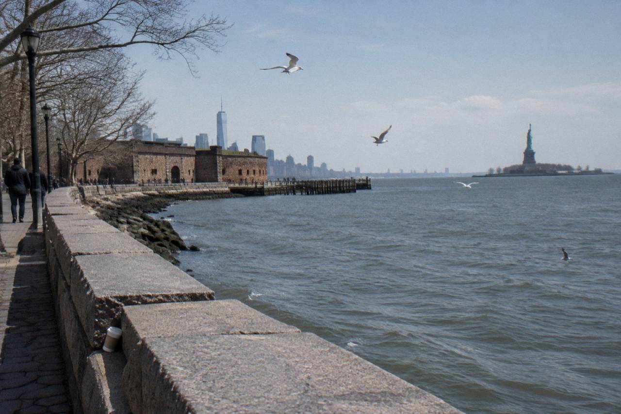The Statue of Liberty on Liberty Island seen across open harbor water from the Manhattan shoreline