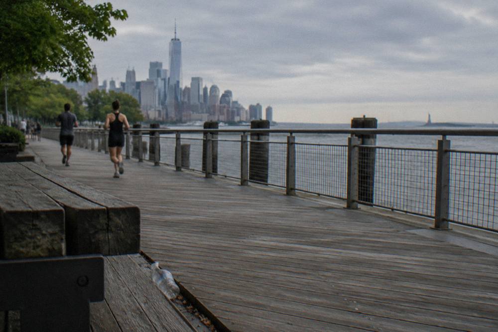The Statue of Liberty in the distance across New York Harbor from a Manhattan waterfront park