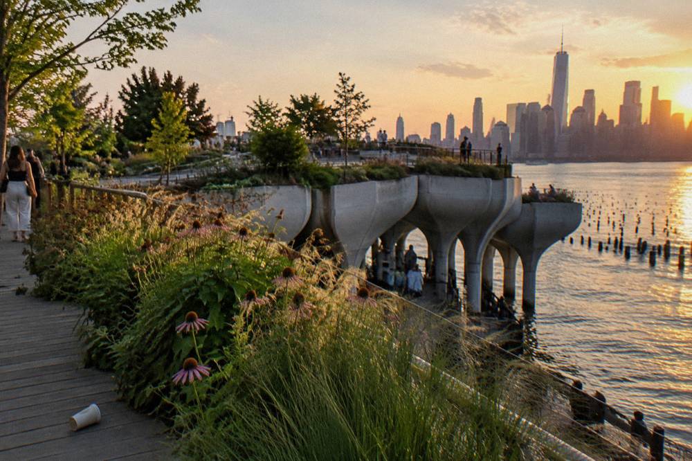Elevated walkway of a planted waterfront park curving over the river with greenery on both sides.