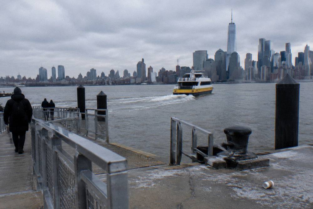 Commuter ferry moving across the river with the Manhattan shoreline and towers behind it.