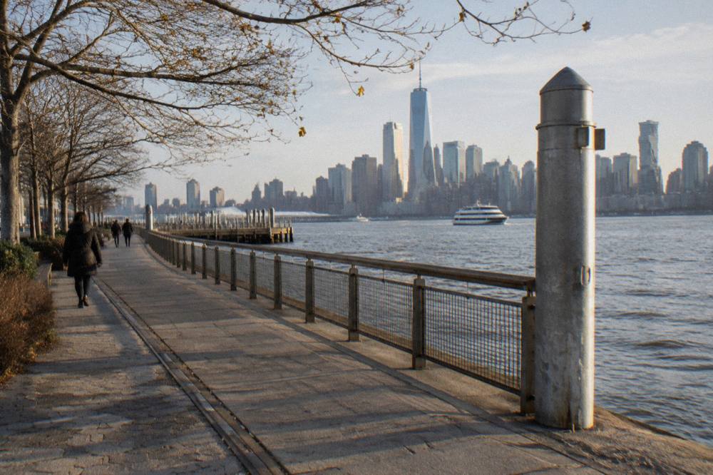 A numbered Hudson River pier sign beside a walkway with the river and a distant cruise boat