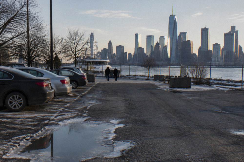 A surface parking lot beside a Hudson River pier with cars parked in rows