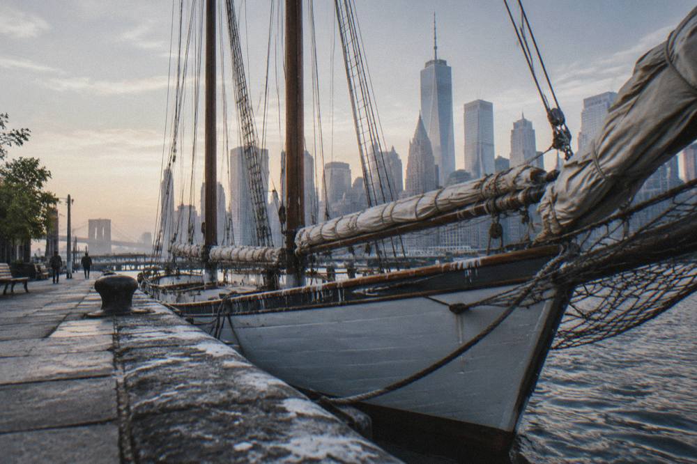 Tall masts of a schooner docked at a pier with the lower Manhattan skyline behind it