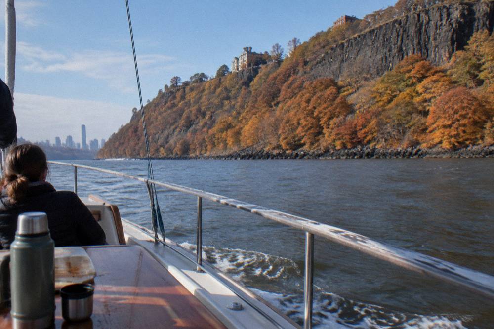 A yacht heading up the Hudson River beside forested Palisades cliffs in autumn color