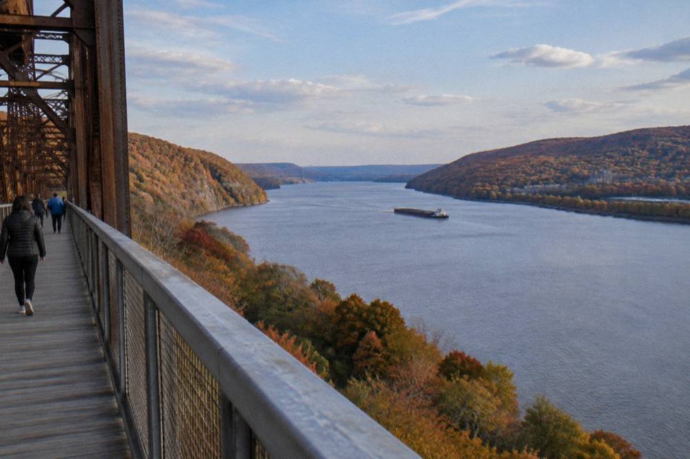 A wide river valley with autumn hillsides in orange and red under a clear afternoon sky