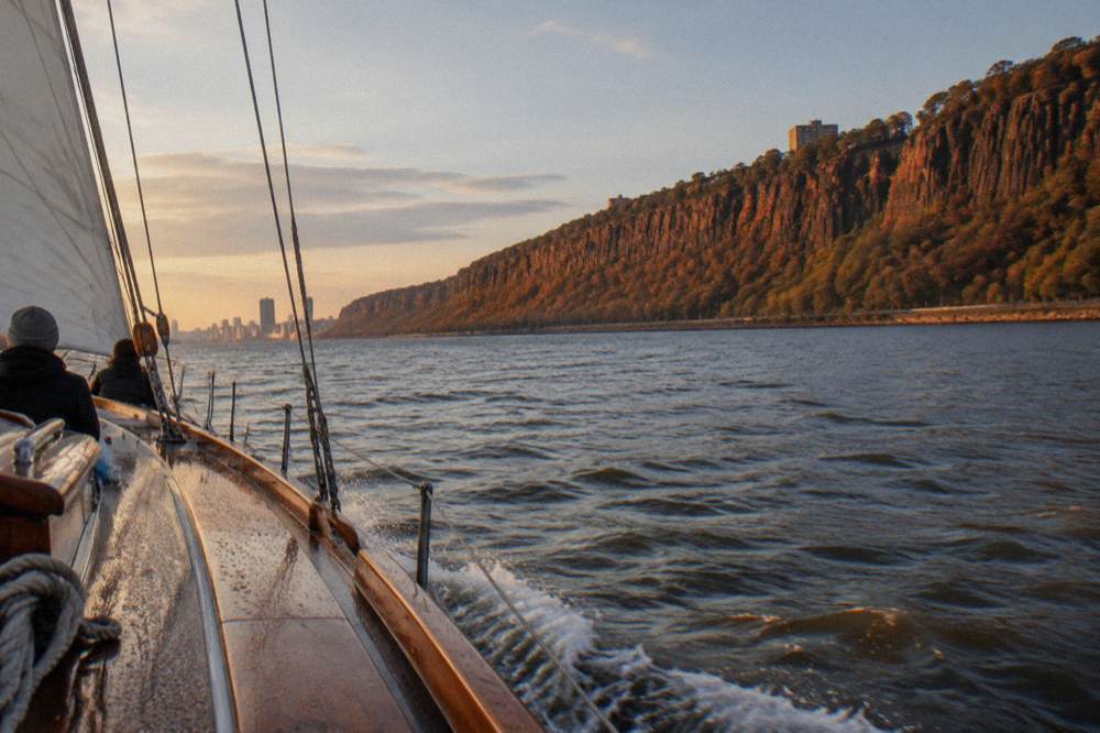 Schooner under sail on open water in late afternoon light with autumn color on the far shore