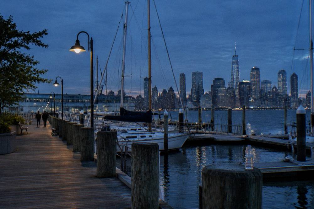 Waterfront pier at dusk with masts of moored sailing vessels visible above the dock