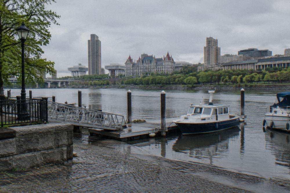 A small ferry landing on a river with a town street and moored boats nearby