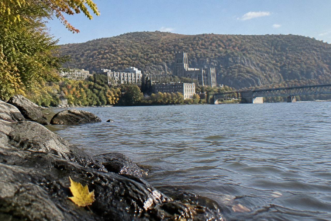 A wide river valley with forested cliffs in autumn color rising above calm water
