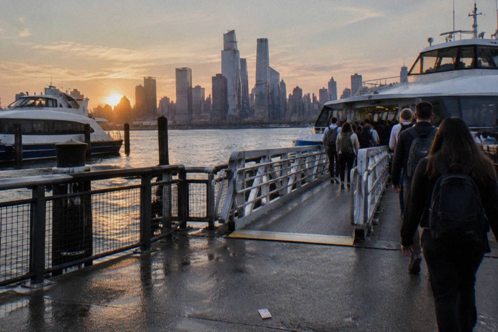 A crowded ferry terminal pier at dusk with boats moored along the Hudson River