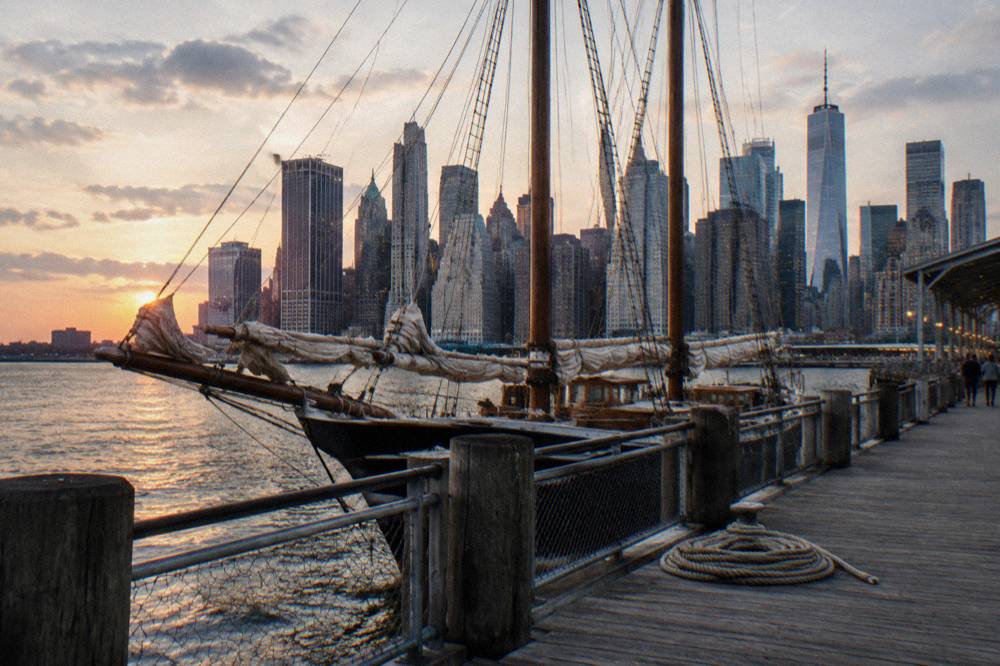 Tall masts of sailing ships along a Manhattan pier with the skyline behind
