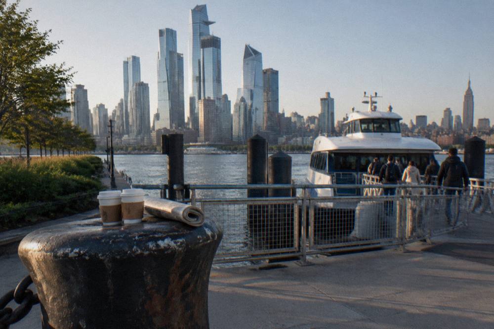 A busy Manhattan cruise pier with a sightseeing boat at the dock and the skyline behind it