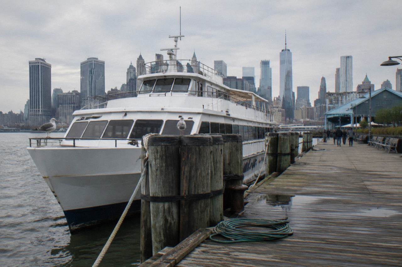 A Hudson River pier in Manhattan with a sightseeing cruise boat docked beside it at midday