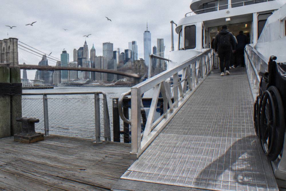 Wide boarding gangway leading from a Hudson River pier to the entrance of a sightseeing boat