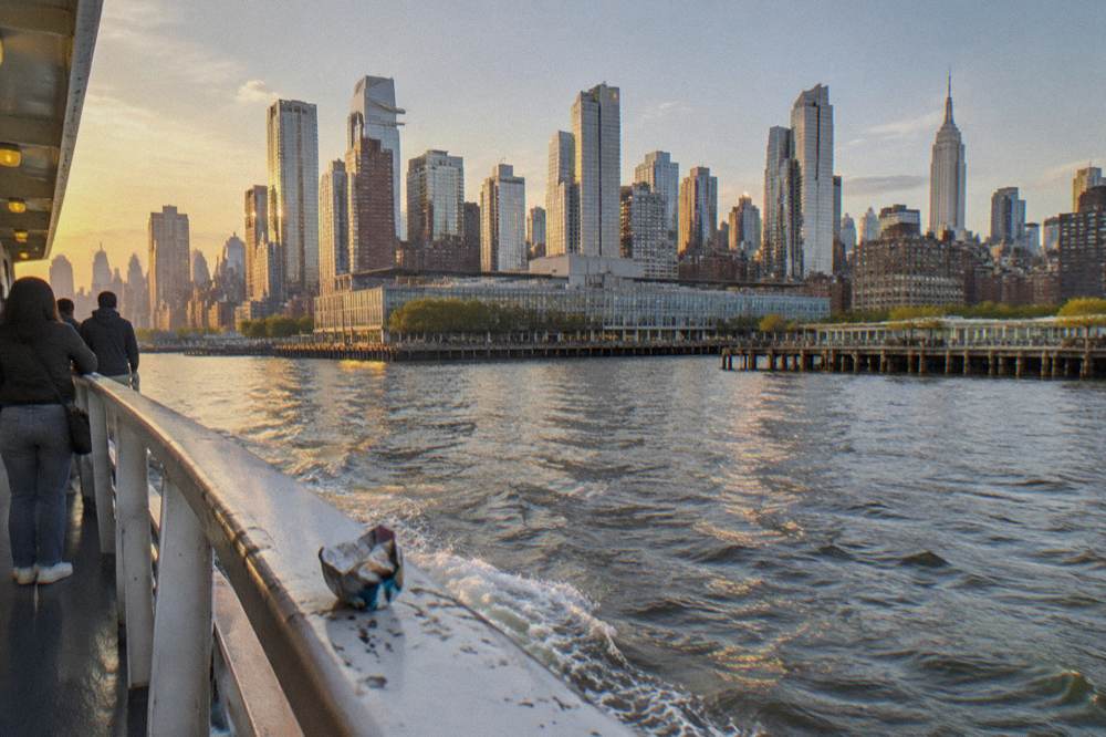 Deck-level view along the rail of a boat with the Manhattan skyline sliding past