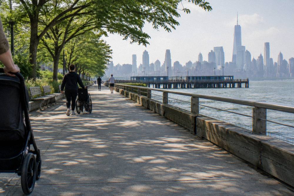Hudson River waterfront path beside a wooden pier with the Manhattan skyline behind it