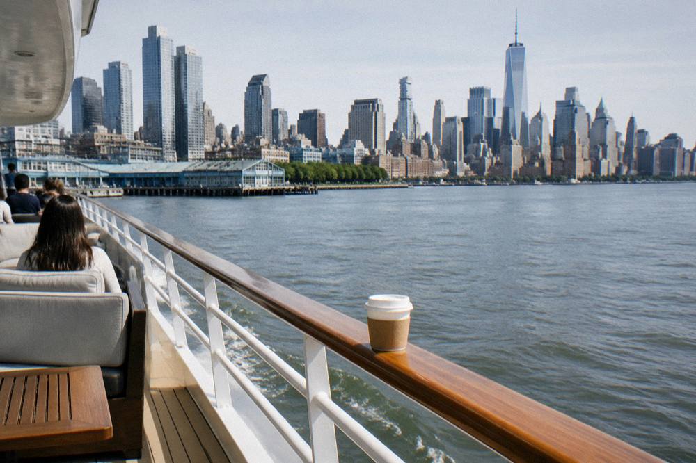 A yacht sailing on calm water in bright morning light with the Manhattan skyline across the river