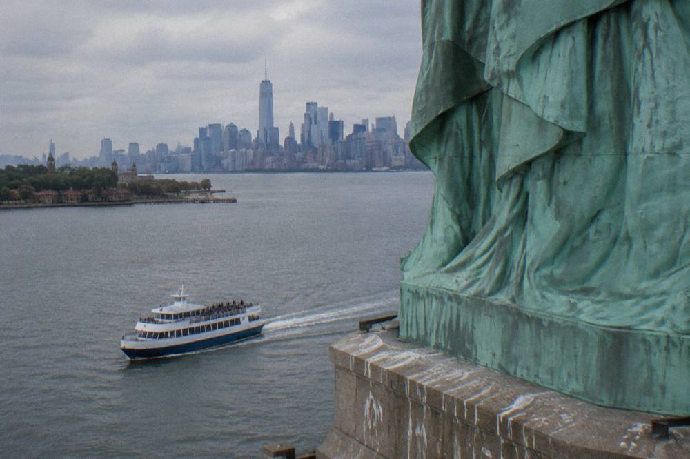 A cruise boat passing close to the Statue of Liberty with the harbor open behind it