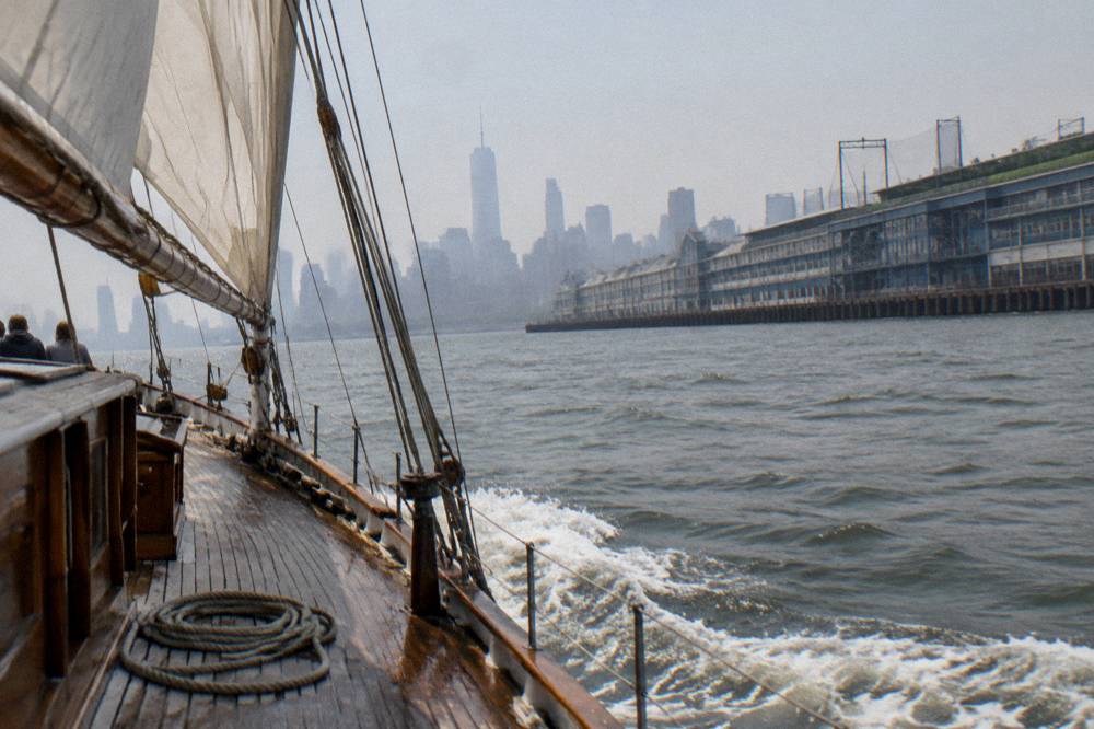 A schooner under sail on the Hudson River with city towers behind it