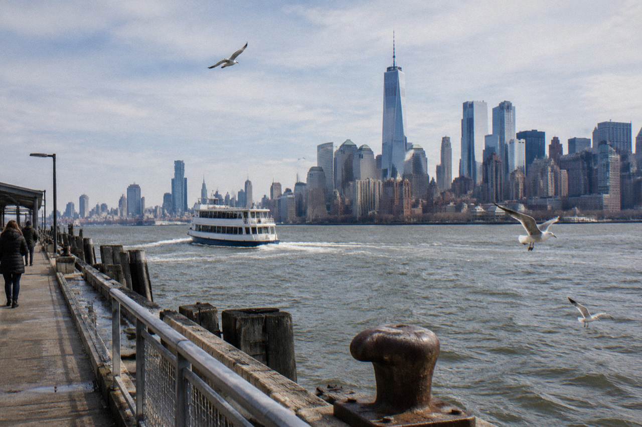 A sightseeing boat on New York Harbor with the Manhattan skyline behind it under a wide sky