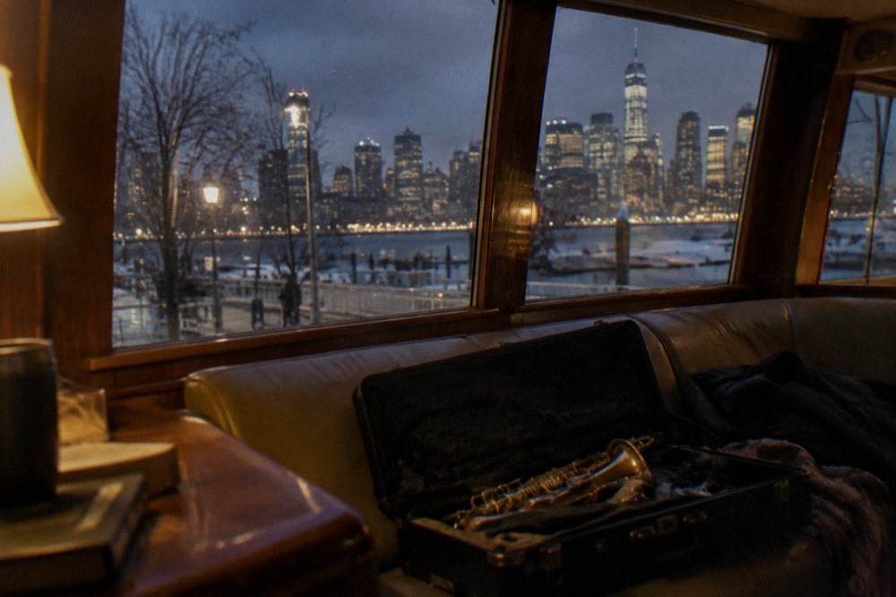 A yacht cabin lit warmly at night with the Manhattan skyline glowing beyond the windows