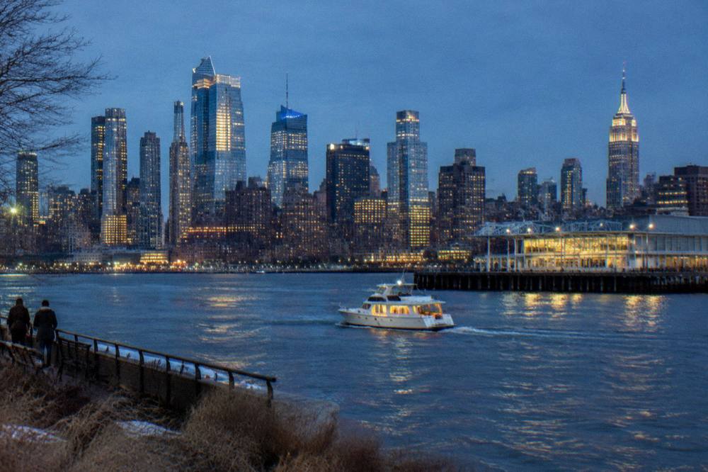 A small motor yacht underway on the Hudson with the city lit up behind it
