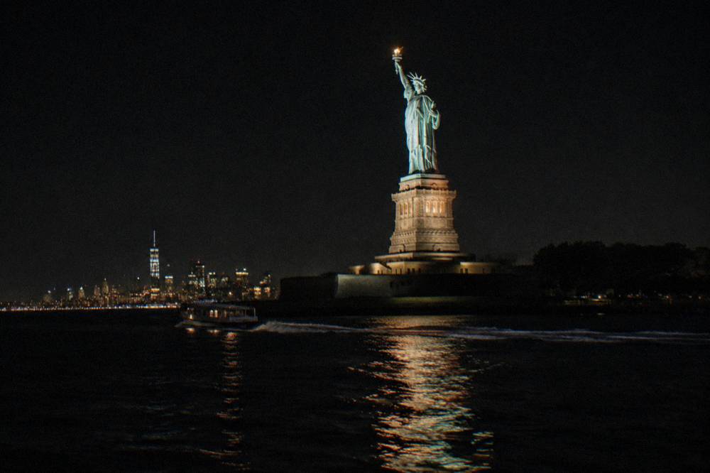 Floodlit Statue of Liberty at night seen from the water with dark sky behind