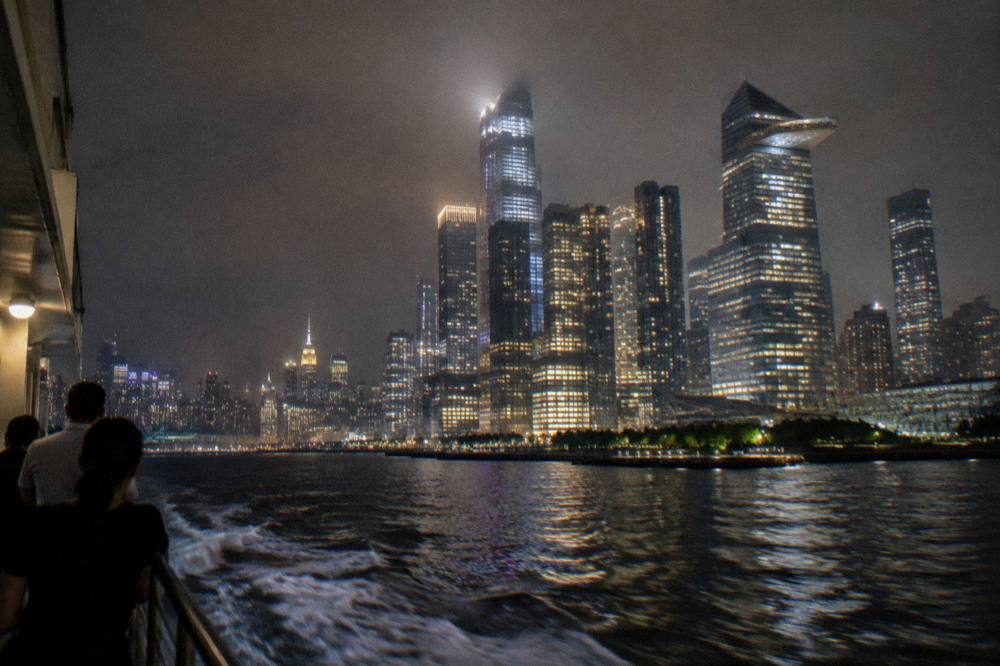 Lit Midtown skyscrapers seen across the Hudson River at night from a boat rail