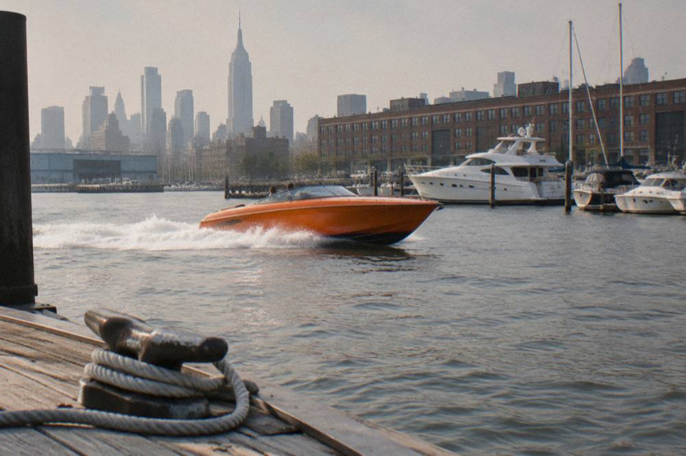 A bright orange speedboat speeding across harbor water with spray at the bow