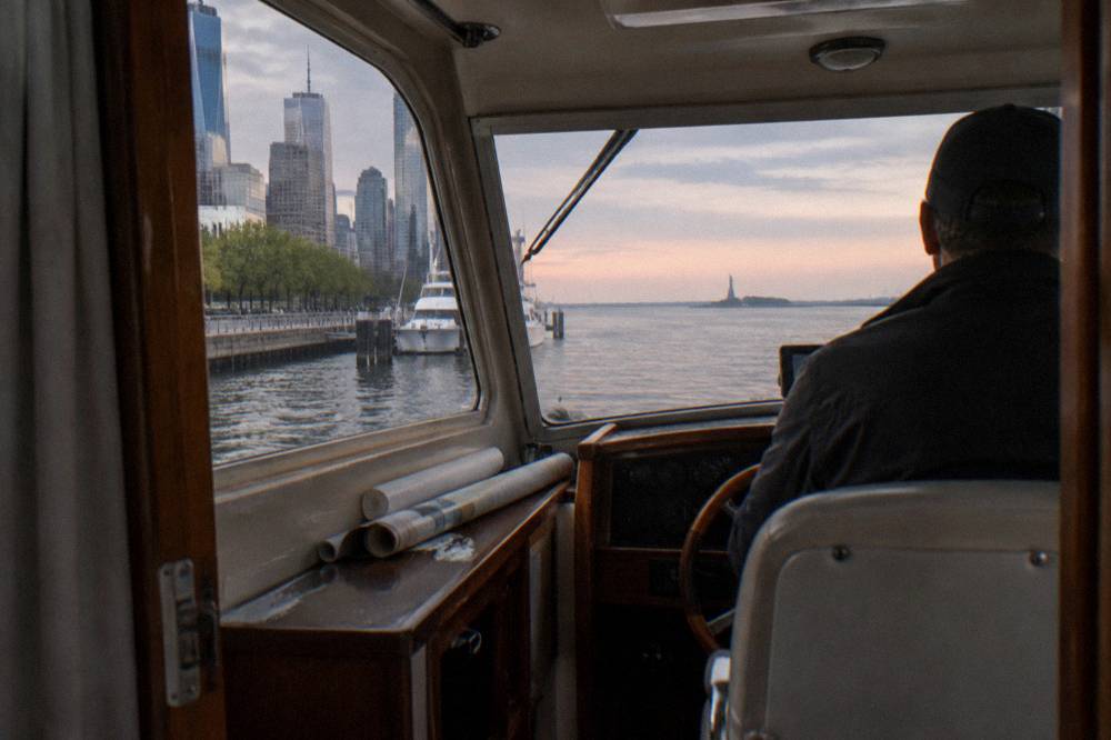A captain at the helm of a small yacht with the Statue of Liberty in the distance
