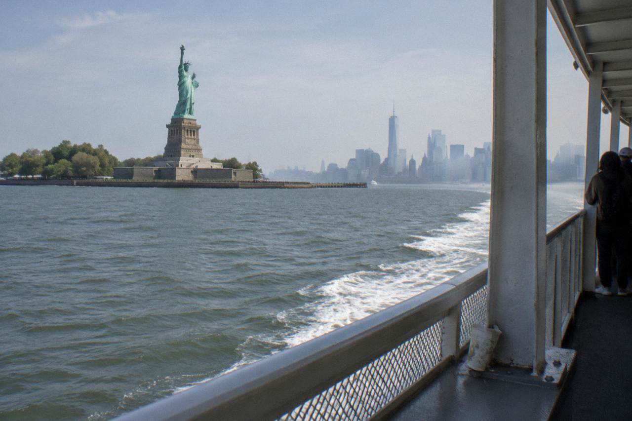 The Statue of Liberty seen from the water at midday with a harbor skyline behind it